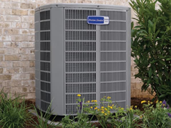 Residential AC Installation in North Texas American Standard air conditioning unit installed outside a brick home with landscaping